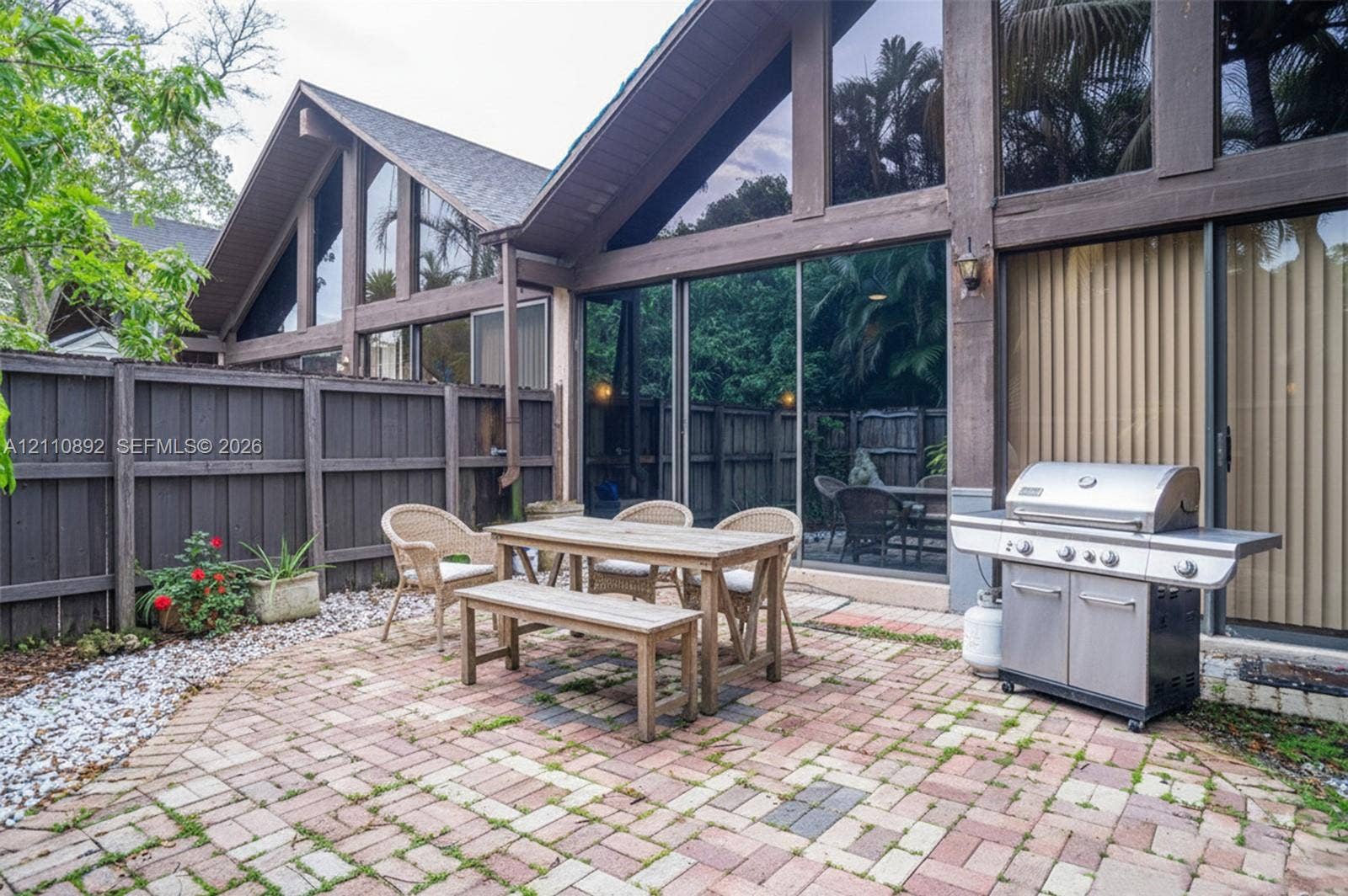 497 N University Drive, #2-7, Plantation, FL 33324 Paved brick patio featuring floor-to-ceiling glass paneling, A-frame architectural design, exterior wood-beam framing, and a perimeter wood fence