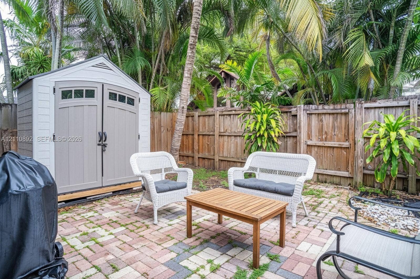 497 N University Drive, #2-7, Plantation, FL 33324 Exterior storage shed with double-door entry, multi-toned paver patio, wood-style privacy fencing, and mature palms