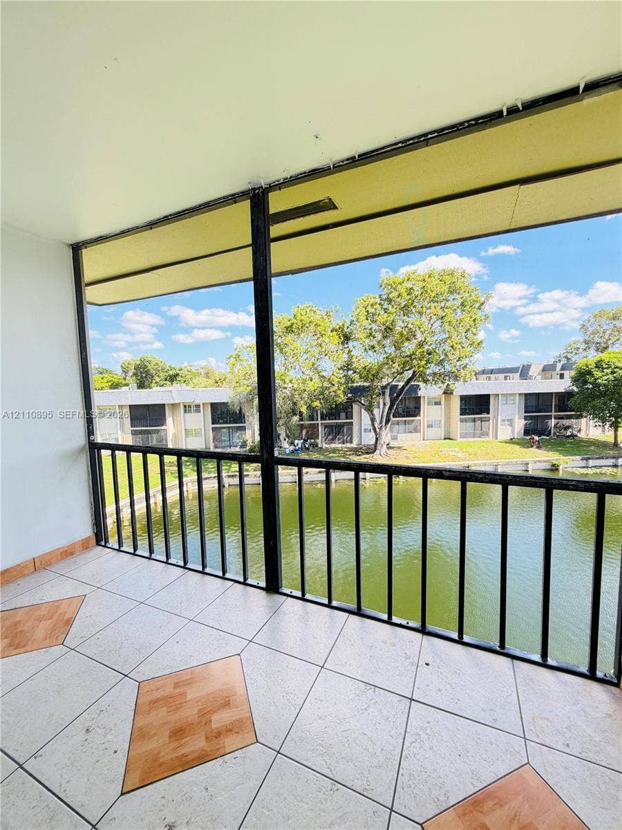 Covered balcony featuring screen enclosure, metal railing, tile flooring with decorative wood-finish accents, and water frontage