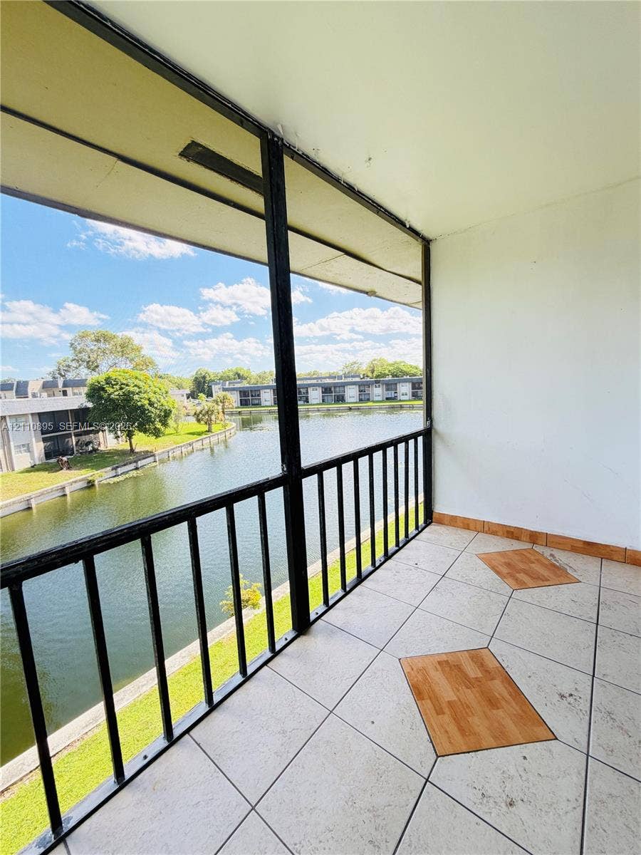 Screened-in balcony featuring ceramic tile flooring with decorative inlay and a metal railing overlooking a water feature