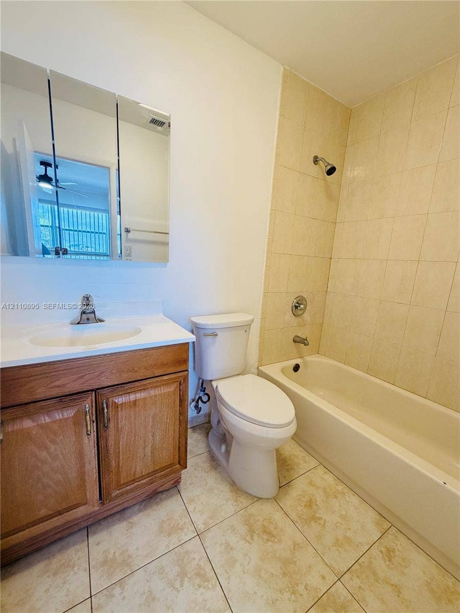 Bathroom featuring a wood-finish vanity with an integrated sink, a multi-panel medicine cabinet, a tiled tub-shower combination, and ceramic tile flooring
