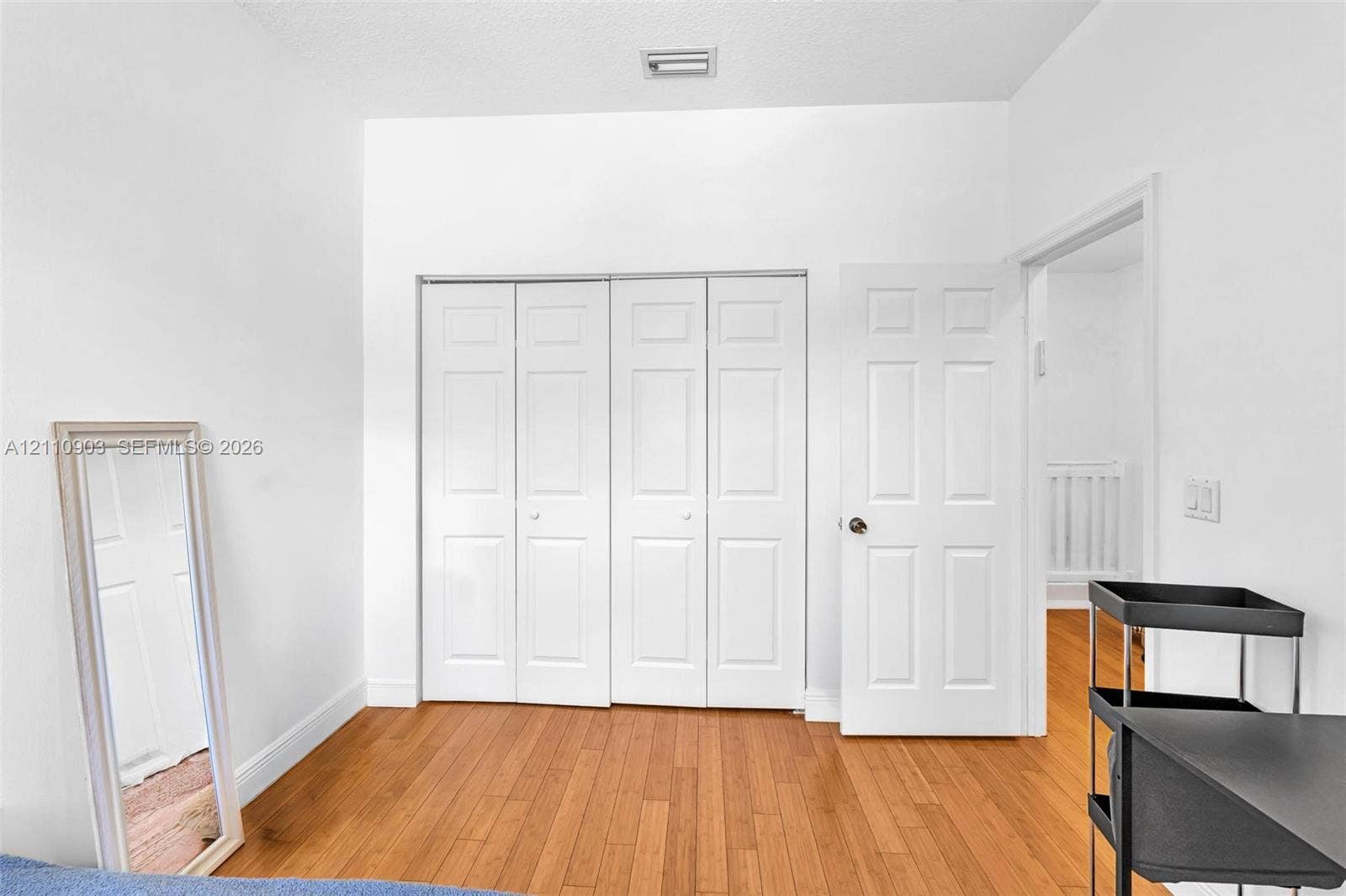 Room featuring wood-finish flooring, white walls, and a four-panel bi-fold closet