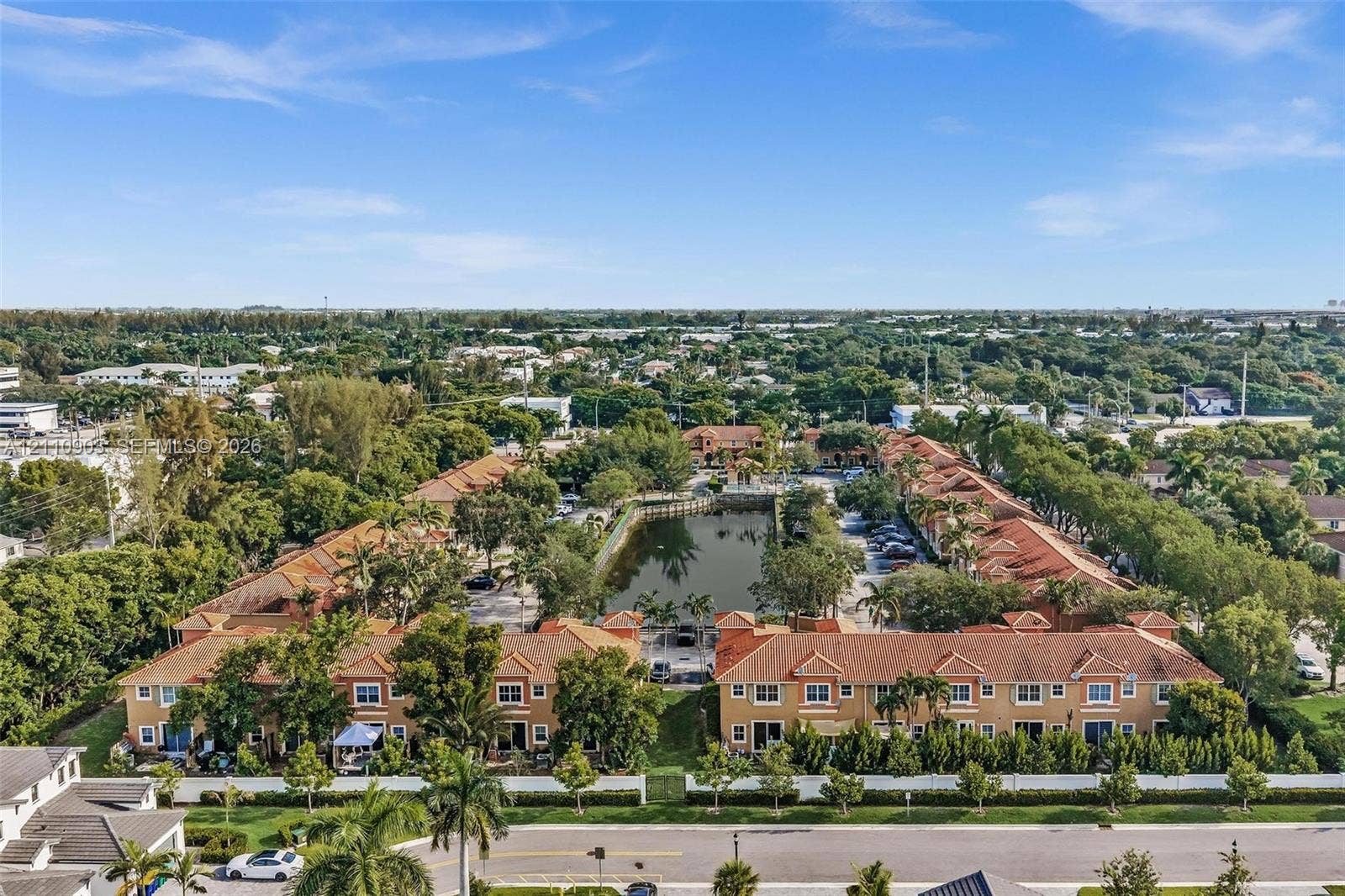 Aerial view of a residential complex featuring multi-story structures with tile roofing, central water feature, and surrounding mature landscaping