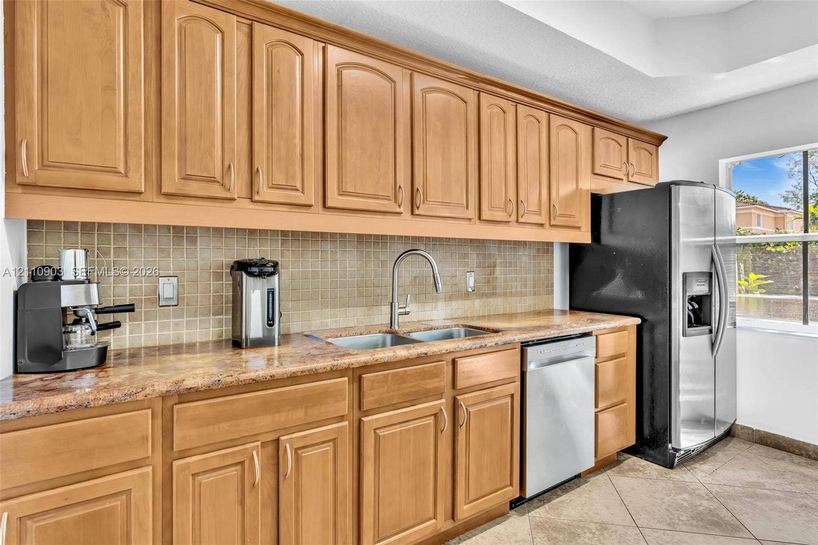Kitchen featuring light-tone wood cabinetry, stone-surface countertops, mosaic tile backsplash, stainless steel dishwasher, and tile flooring