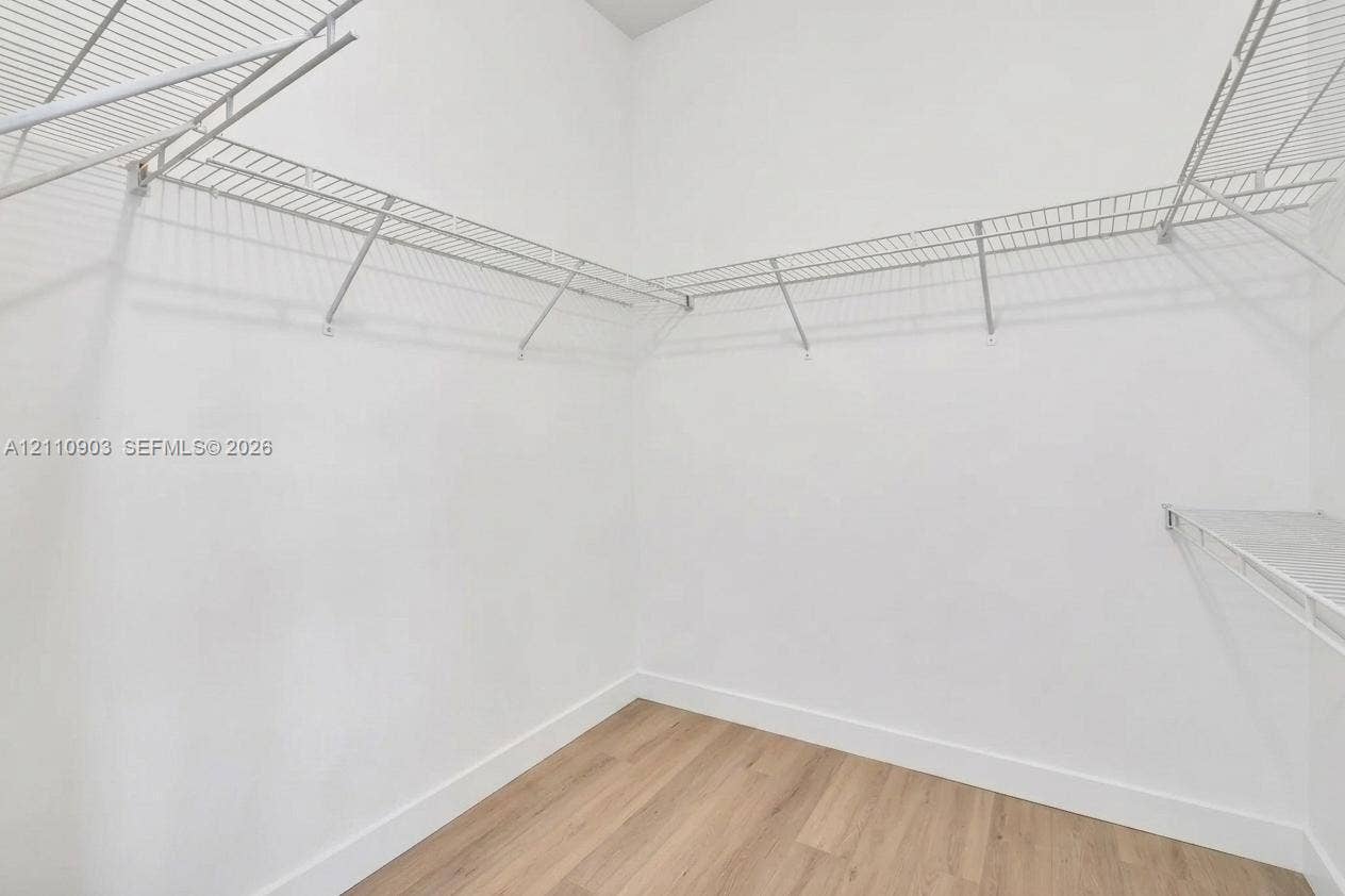 Walk-in closet featuring neutral white walls, wood-finish flooring, and multi-tier wire shelving