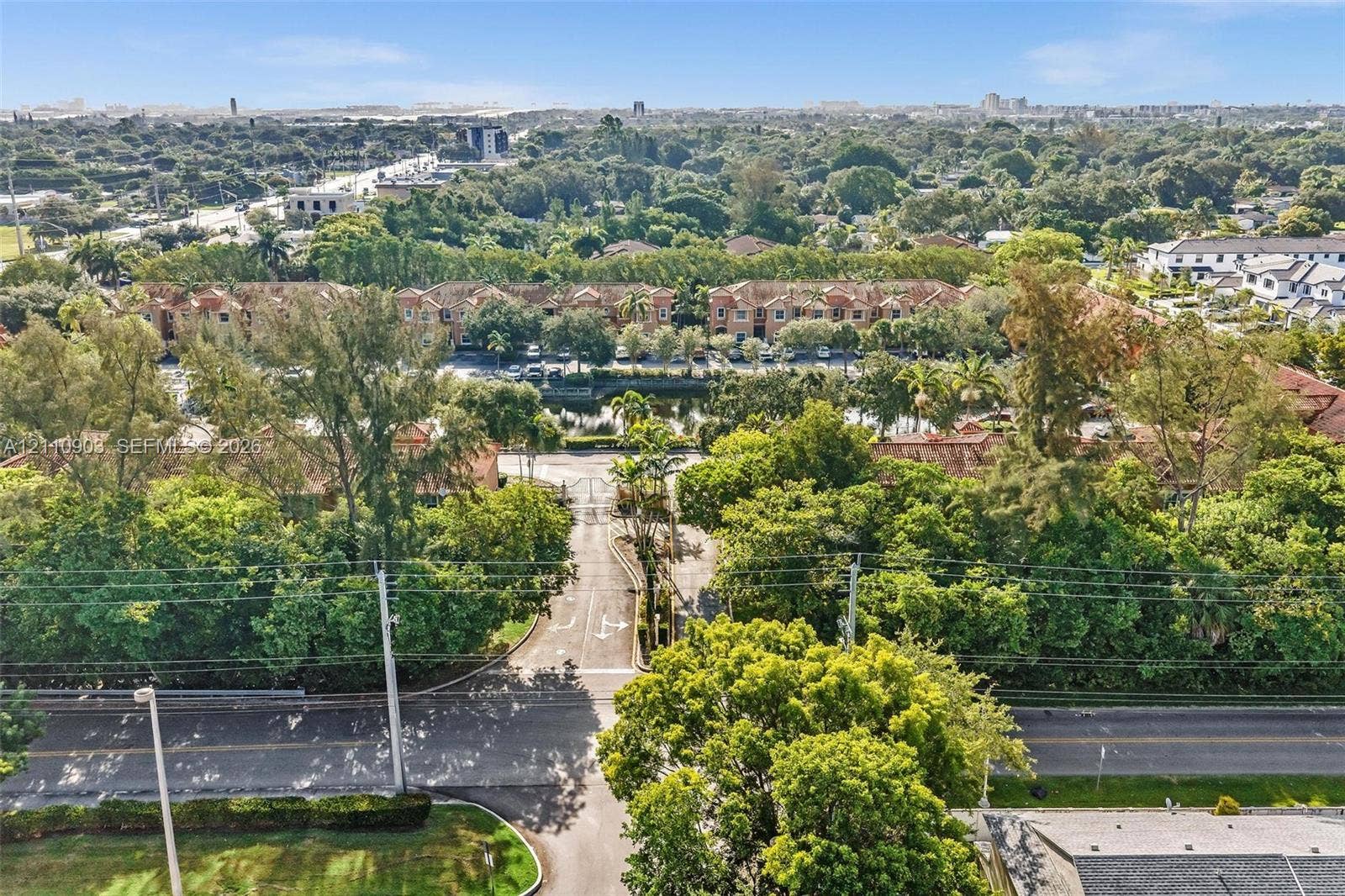 Aerial perspective of the property featuring gated site access, paved private driveways, surrounding mature canopy trees, and an onsite waterway