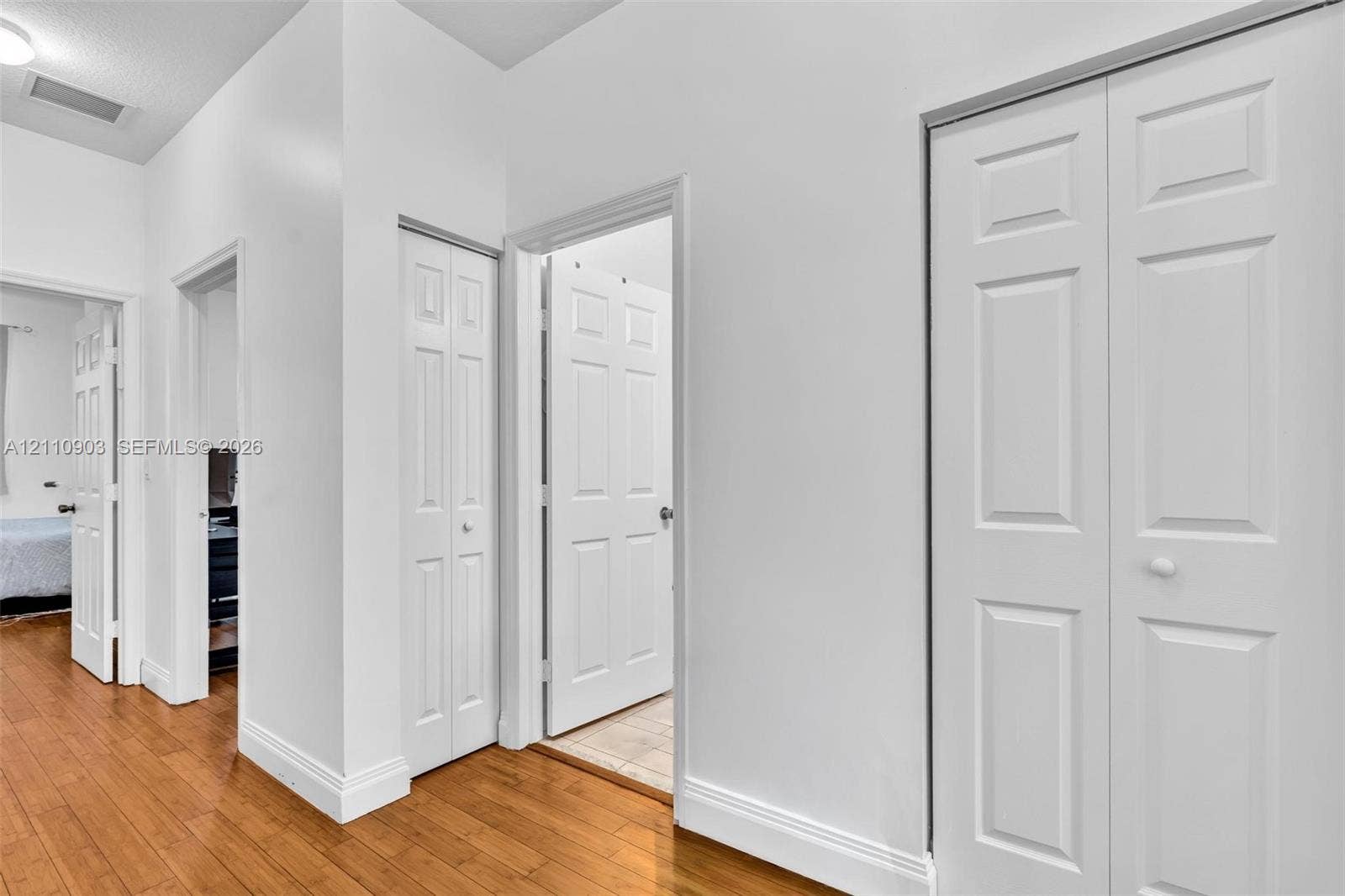 Interior hallway featuring wood-finish flooring, white walls, and multiple bi-fold closet doors