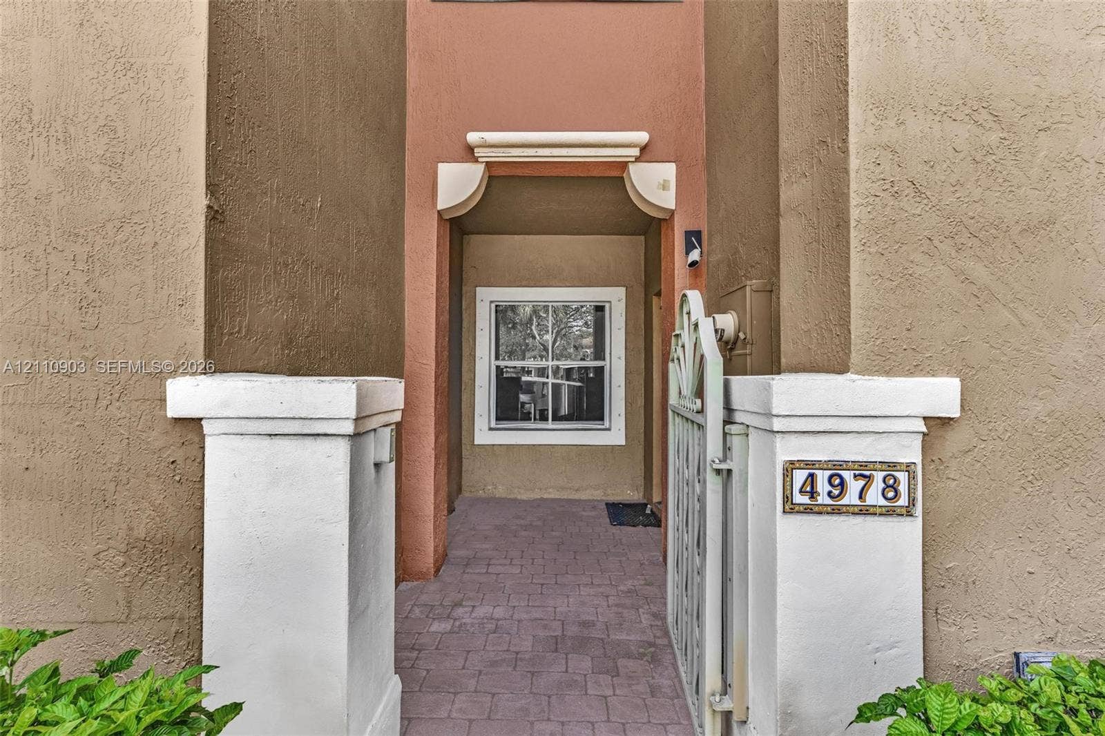 Stucco exterior entrance featuring white pillar bases, decorative metal gate, paver flooring, and arched architectural detailing