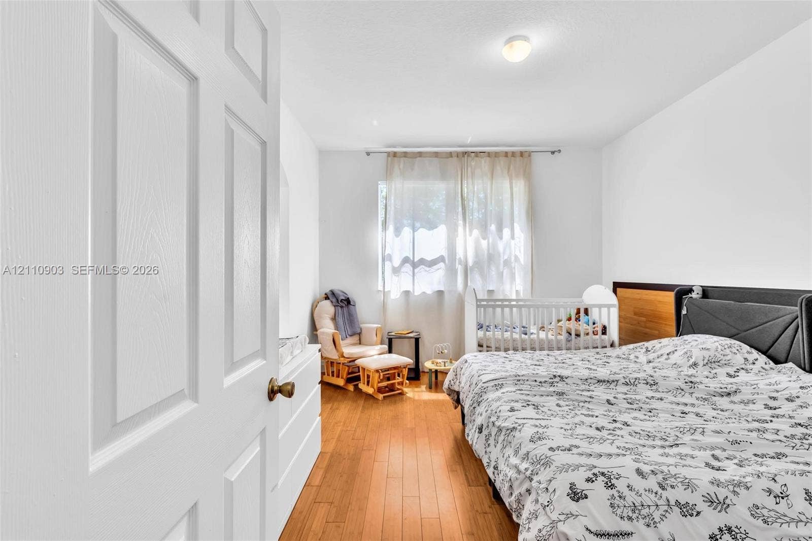 Interior space featuring wood-finish flooring, white walls, a flush-mount ceiling light, a large window, and a paneled interior door