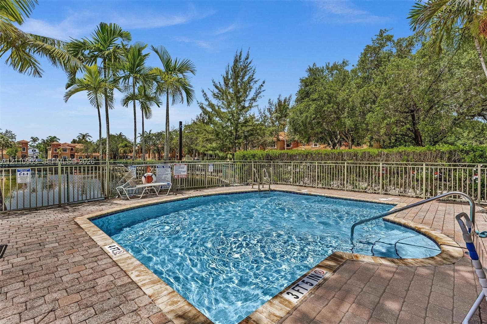 In-ground swimming pool featuring a brick paver deck, metal safety fencing, and a built-in step entry with a stainless steel handrail