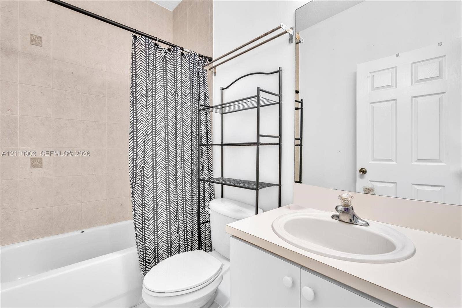 Bathroom featuring a tub-shower combination with floor-to-ceiling beige tile surround, vanity with an integrated oval sink, and a large frameless wall-mounted mirror