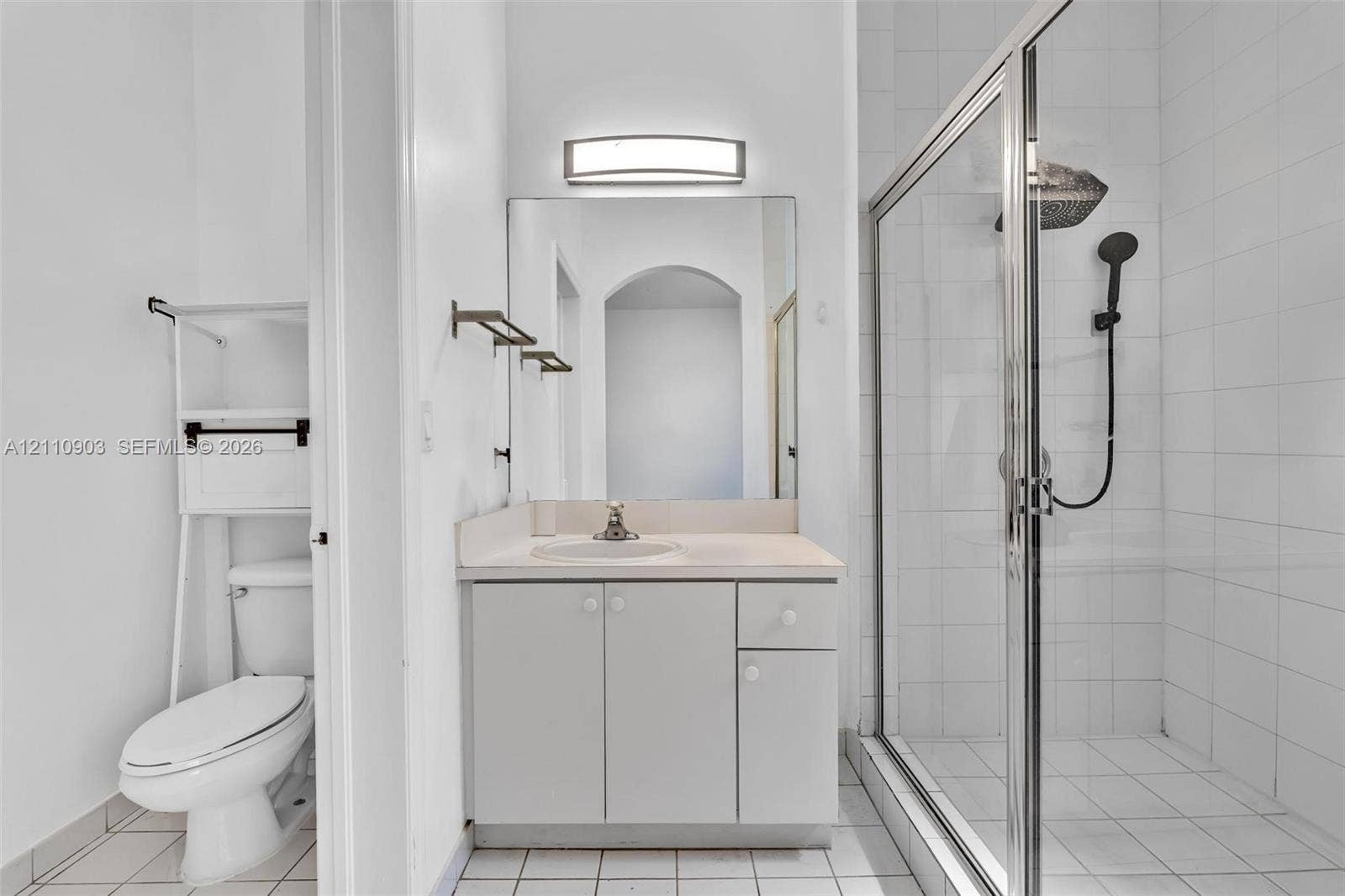Bathroom featuring a vanity with integrated sink, rectangular wall-mounted light fixture, and a glass-enclosed shower with a handheld showerhead and wall-mounted tile surround