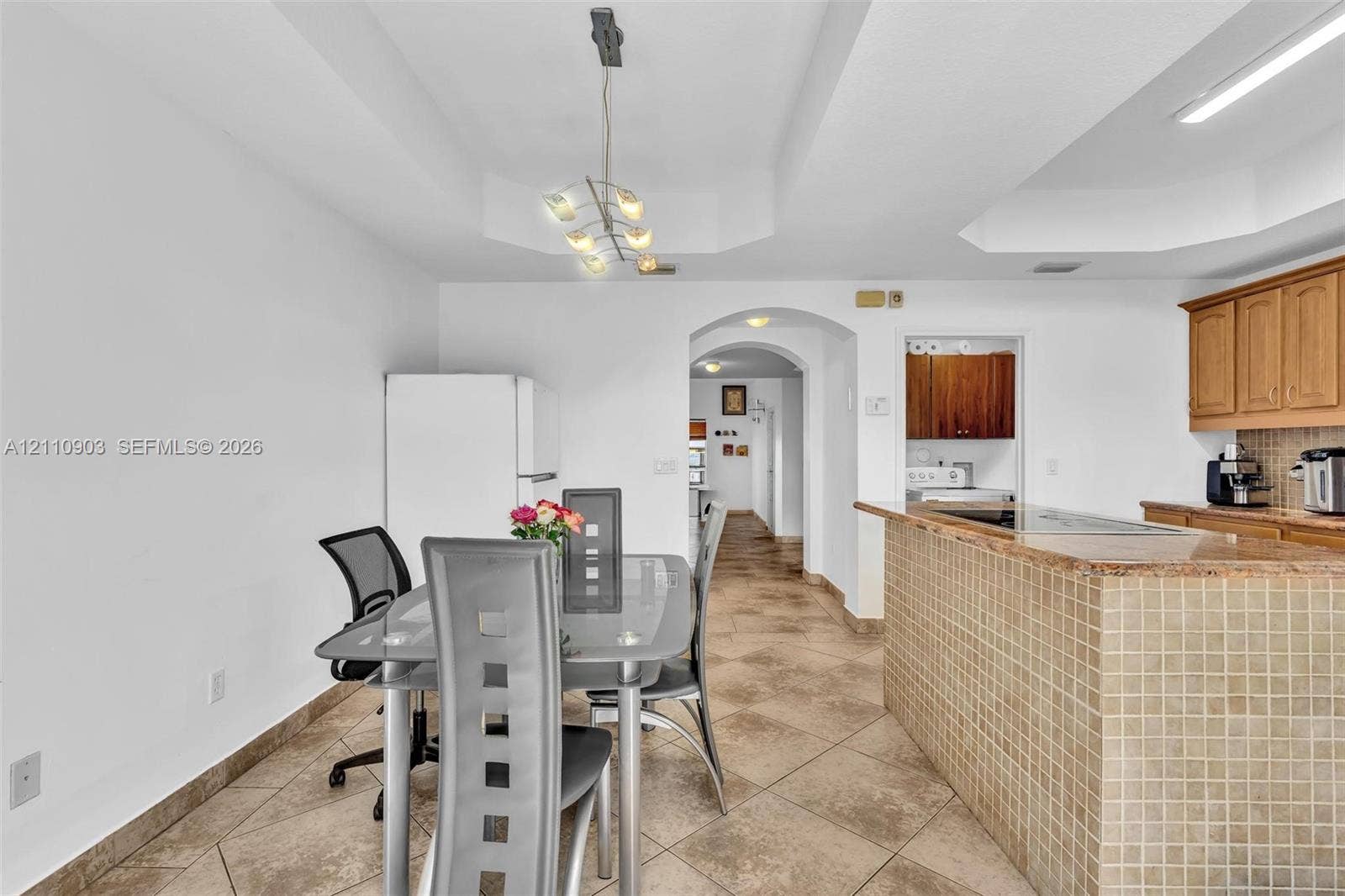 Kitchen featuring stone-finish tile flooring, tray ceilings, recessed lighting, and a center island with a tiled base and stone-finish countertop