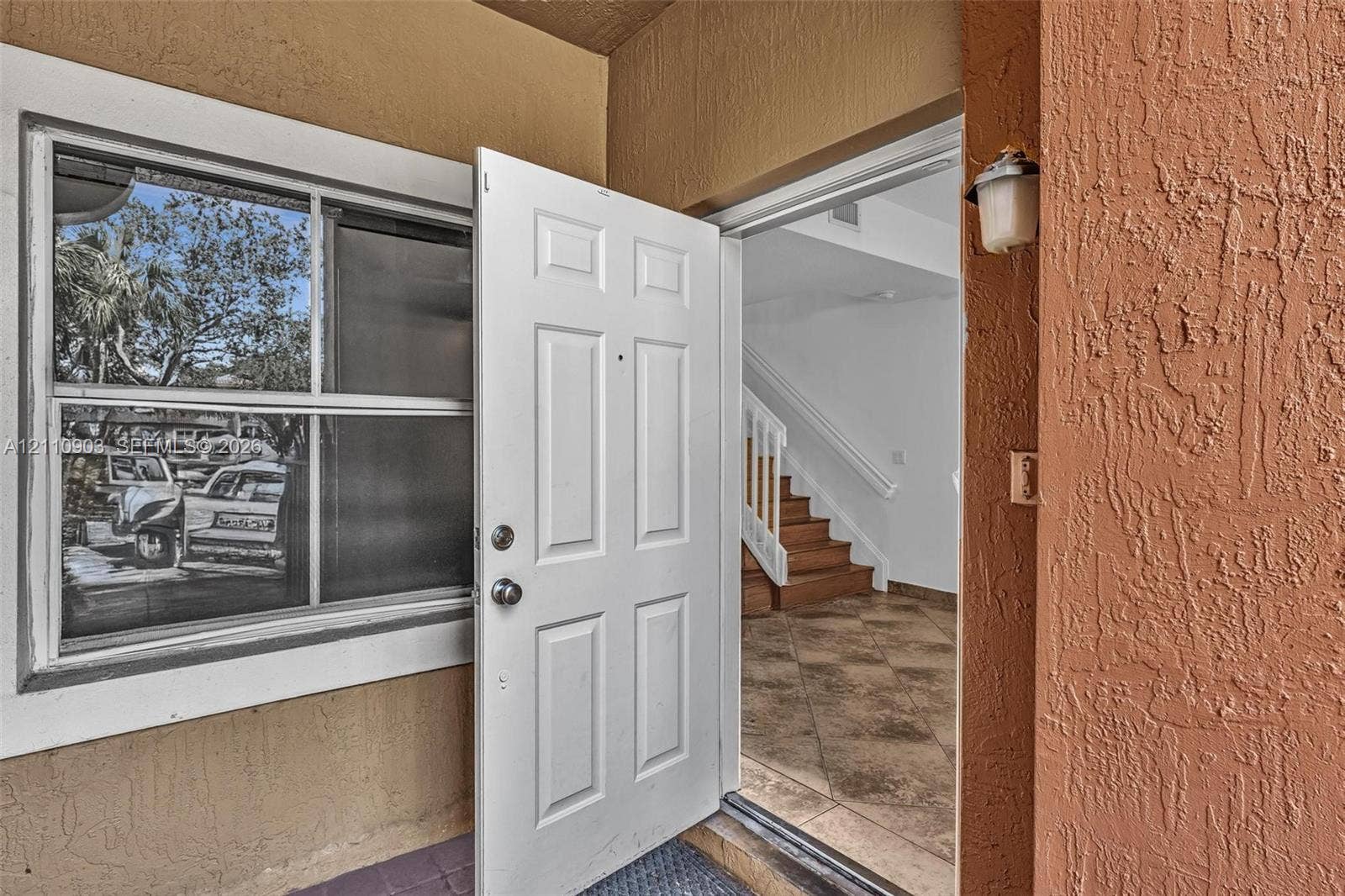Stucco exterior entryway featuring a multi-panel front door, decorative wall-mounted lighting, and a single-hung window with a light-colored frame
