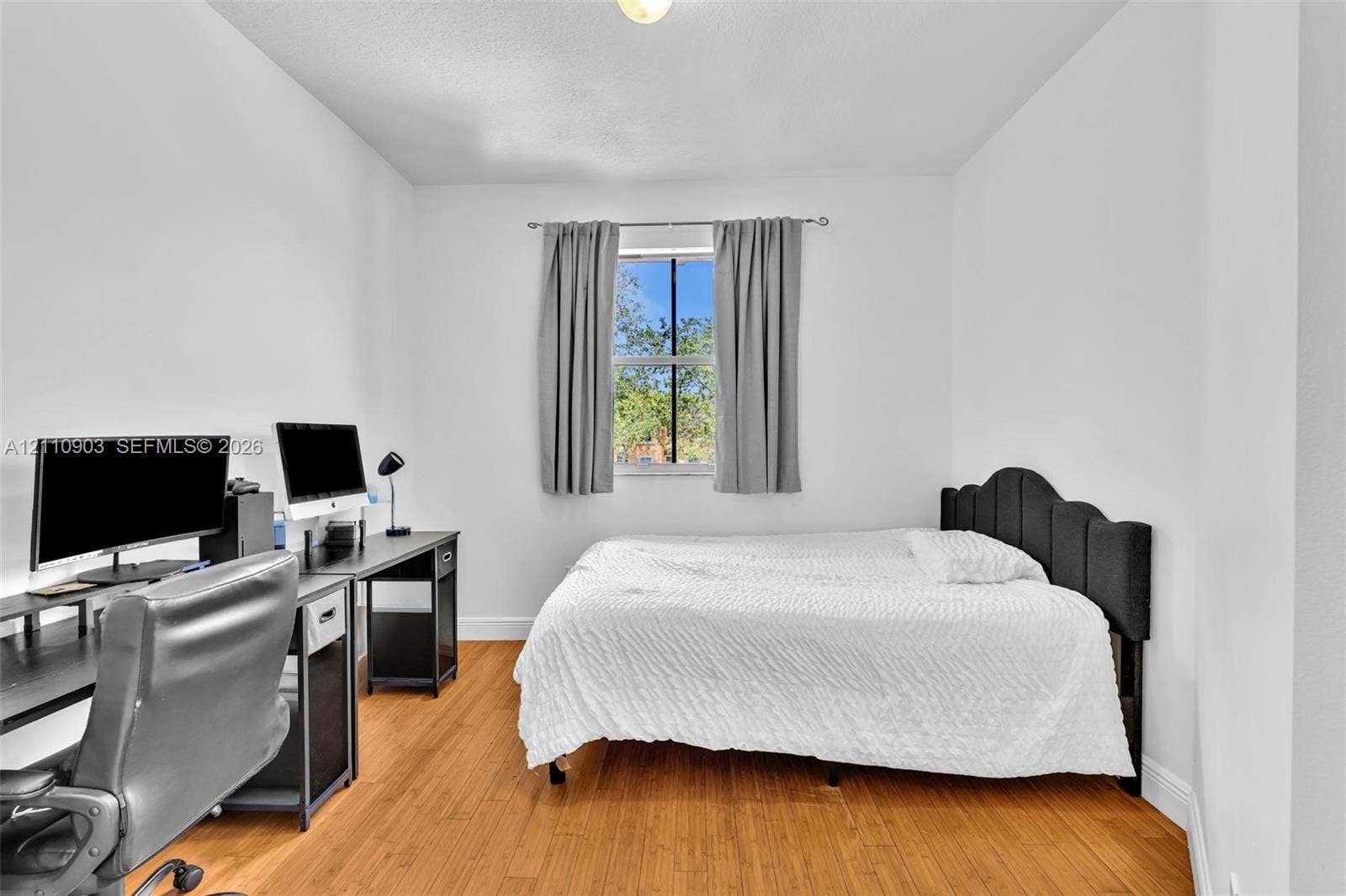 Bright room featuring wood-finish flooring, white walls, and a window with a metal rod
