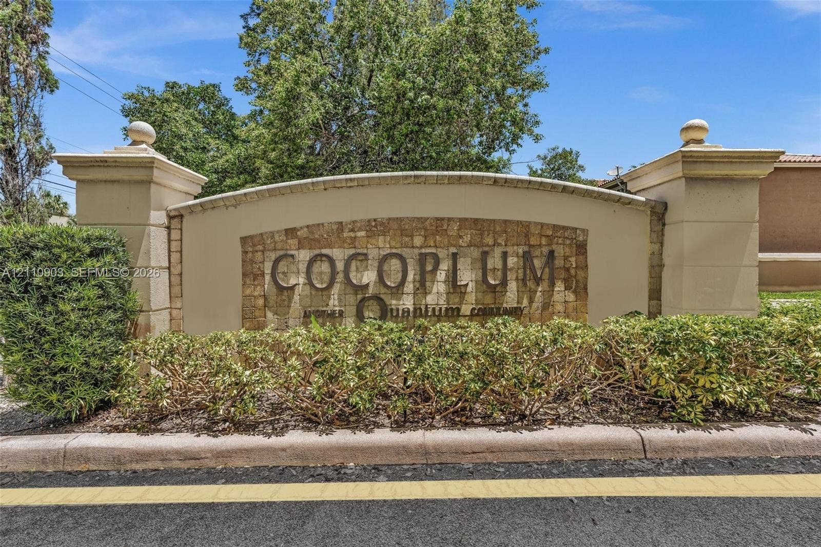 Custom monument entrance featuring a textured stone facade, tiered stucco pillars with capstones, and manicured landscaping