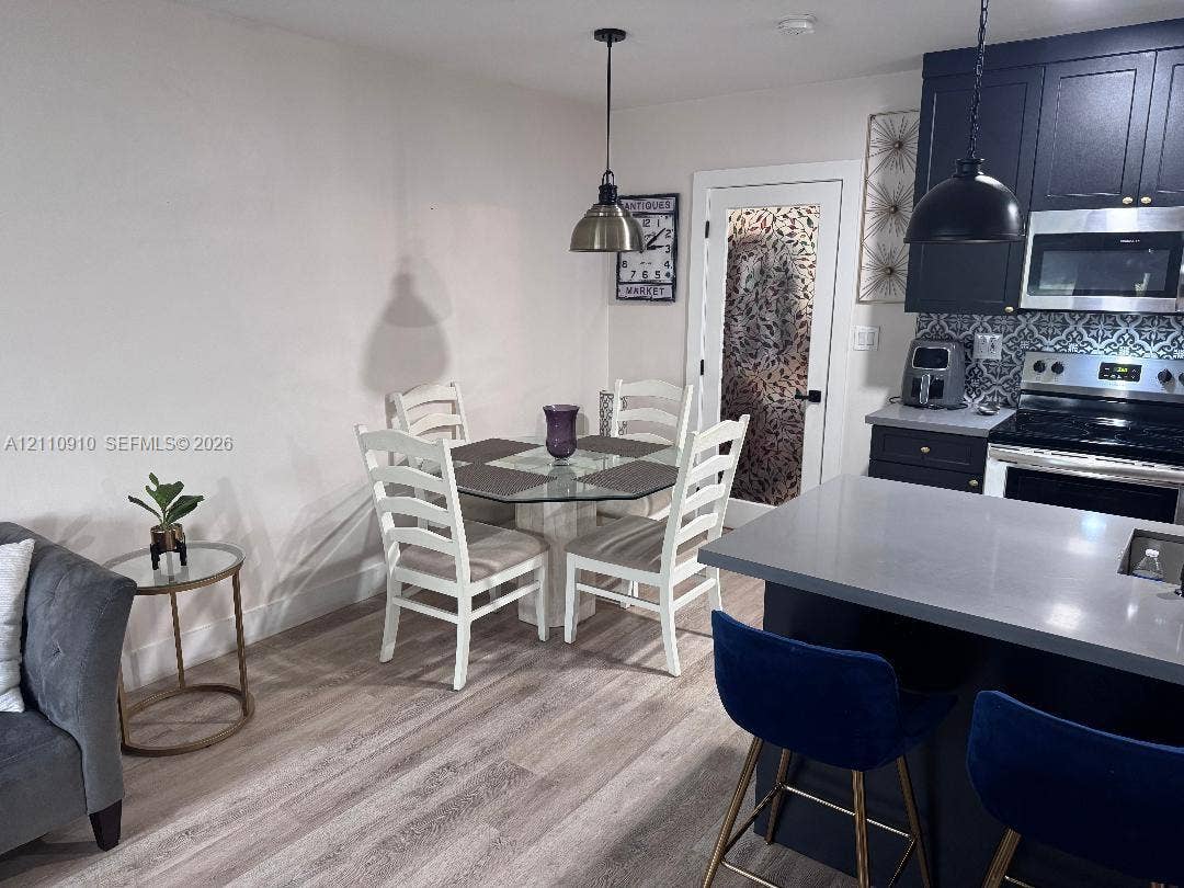 Kitchen featuring dark cabinetry, solid-surface countertops, decorative backsplash, wood-finish flooring, and dual hanging pendant lights