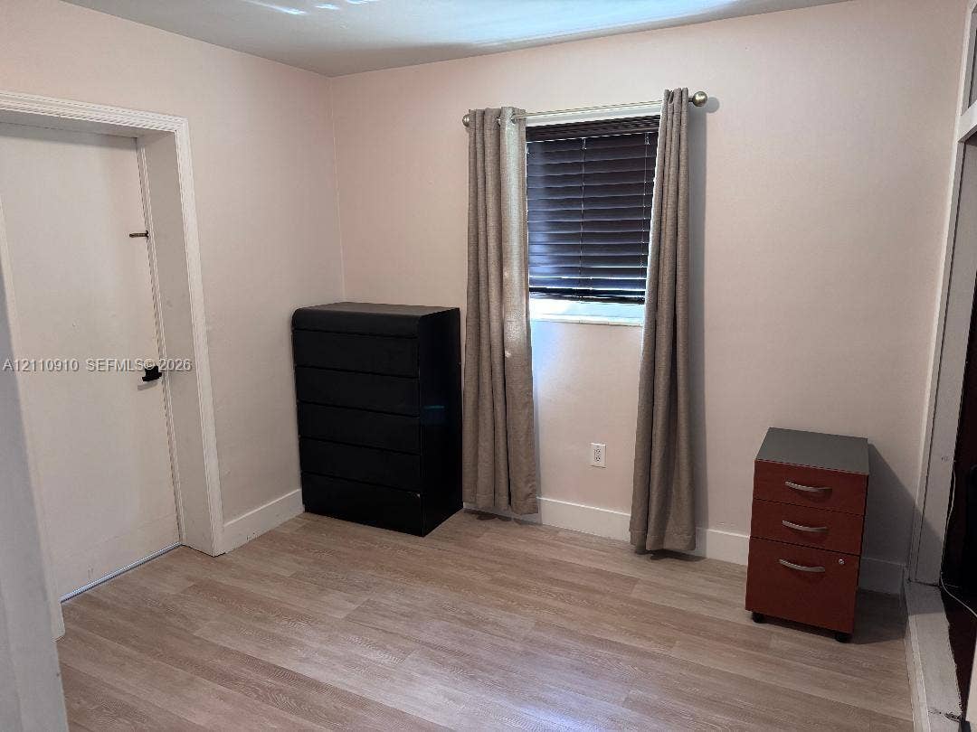 Room featuring wood-finish flooring, a single-hung window with horizontal blinds, and a standard interior door with an arched doorway casing