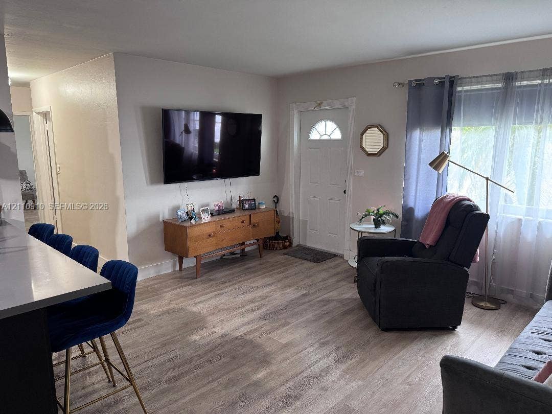 Living area featuring wood-finish flooring, a neutral color palette, a multi-lite entry door, and a built-in kitchen peninsula with a stone-surfaced countertop