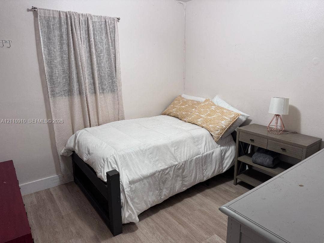 Neutral-toned room featuring wood-finish flooring and a single-window configuration with an installed curtain rod