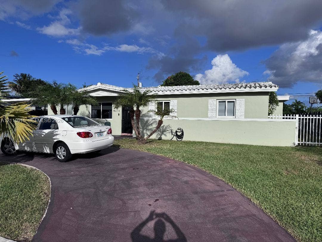 Single-story residence featuring a tile roof, light-colored exterior finish, masonry perimeter wall, white metal fencing, and a curved paved driveway