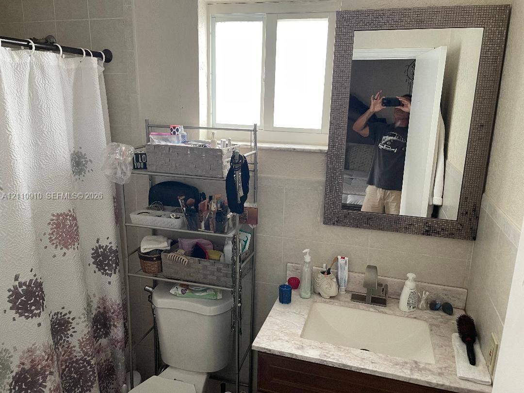 Bathroom featuring a single-sink vanity with a stone-composite countertop, integrated rectangular basin, tiled wall surround, and a framed wall-mounted mirror