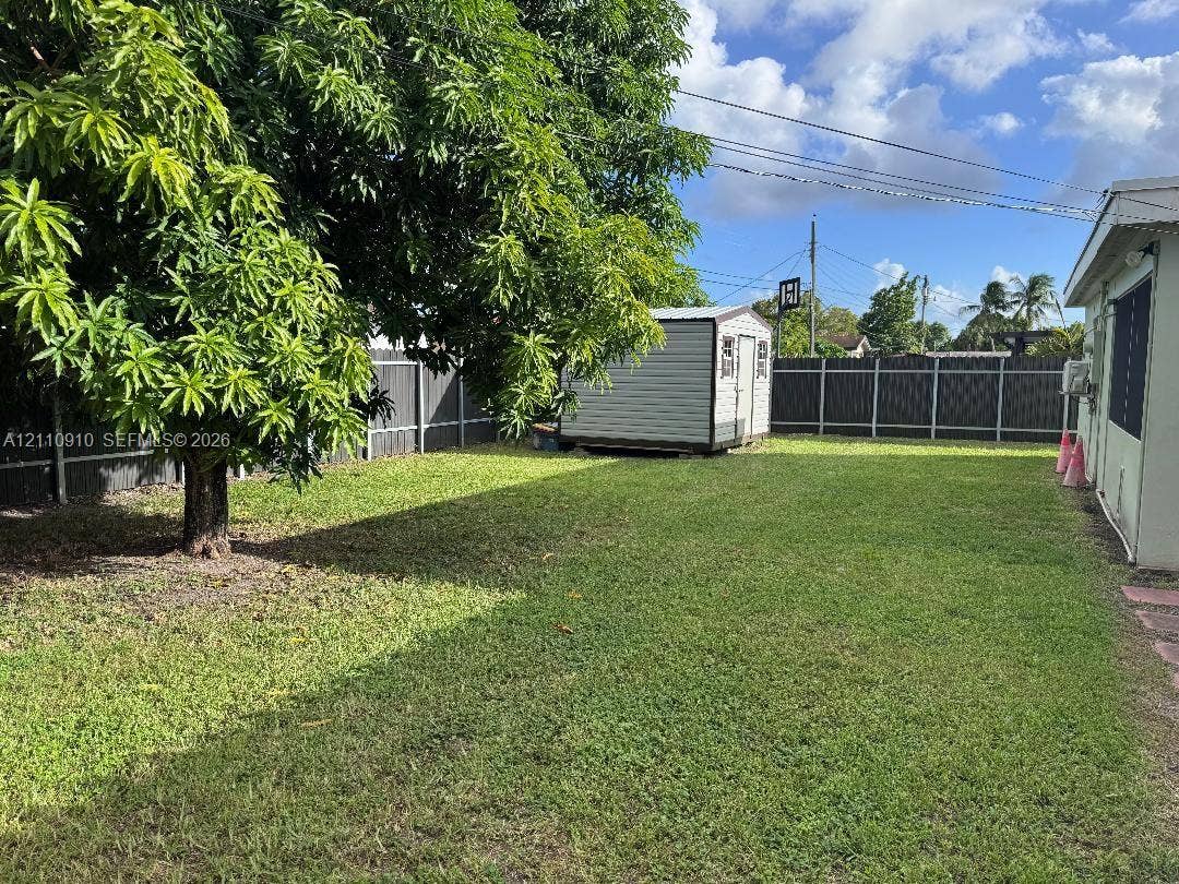 Backyard featuring a grass lawn, mature tree, standalone storage shed, and full-perimeter privacy fencing