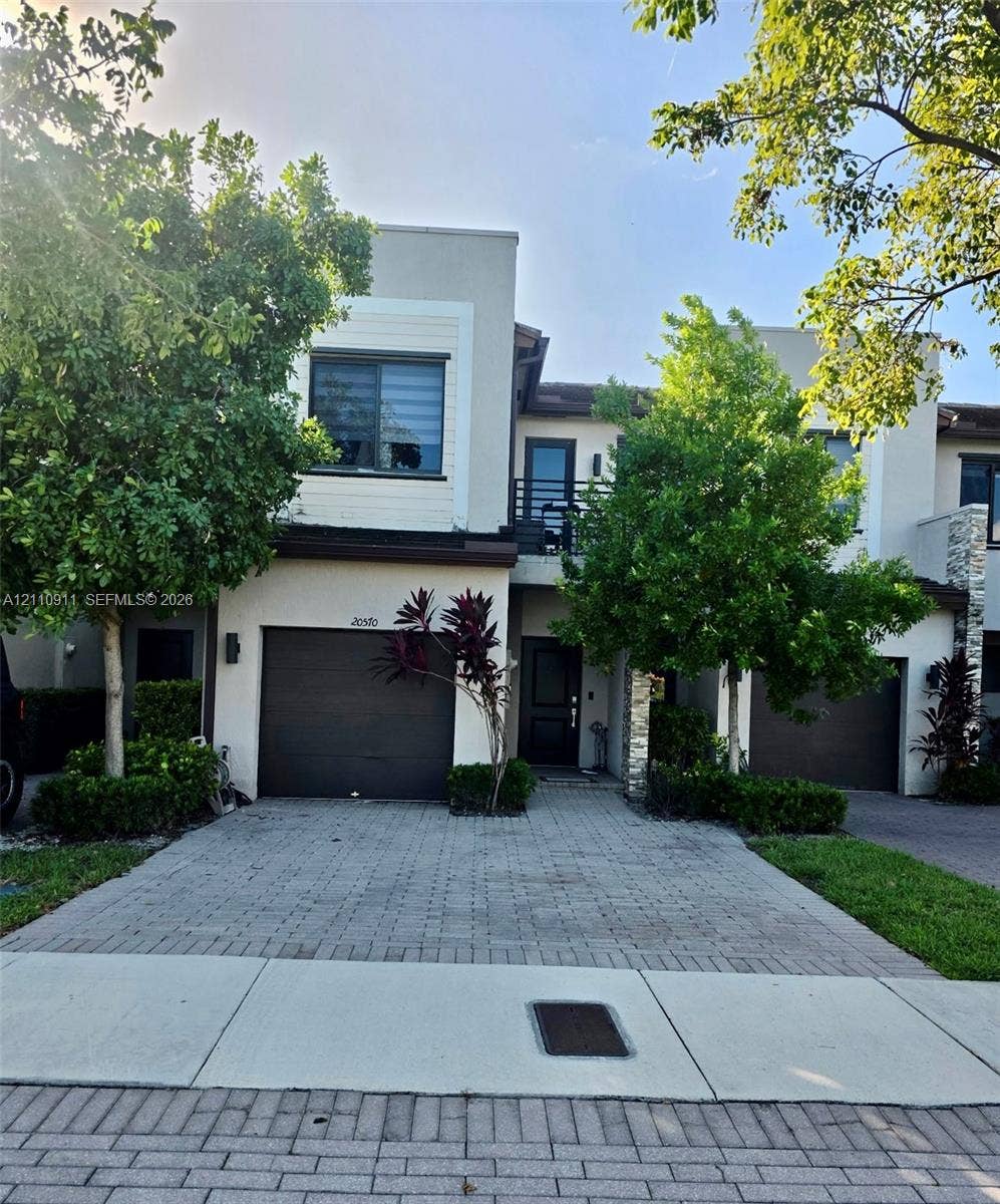 20570 NE 2nd Court, Miami, FL 33179 Contemporary exterior featuring stucco siding, stone veneer accents, a paved driveway, and an attached garage