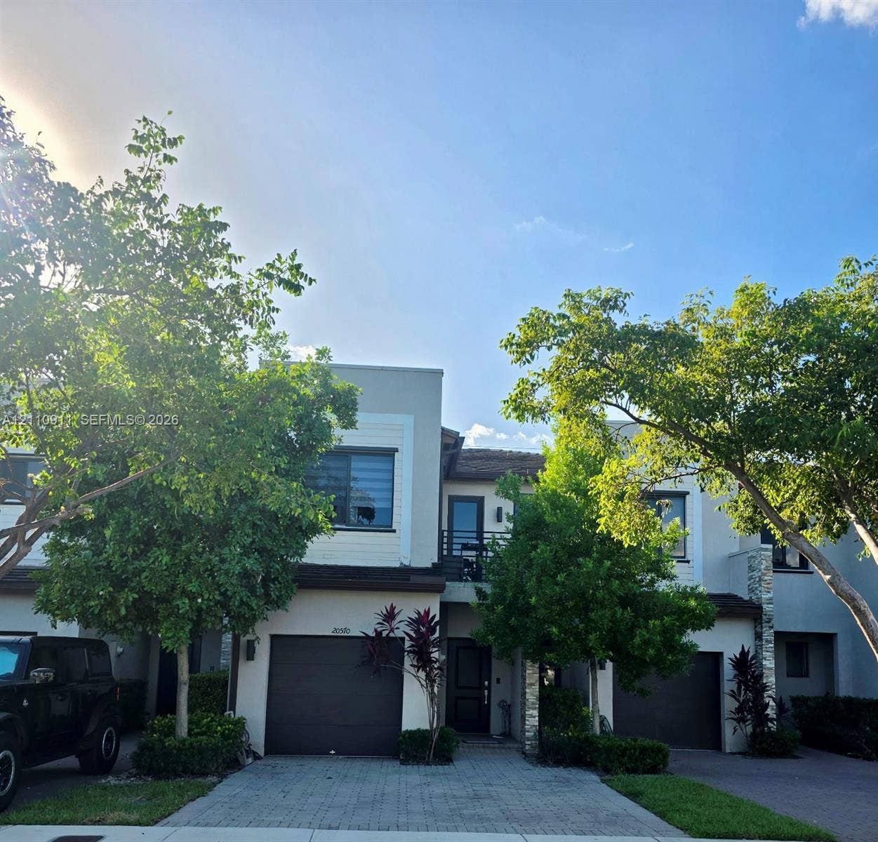 20570 NE 2nd Court, Miami, FL 33179 Contemporary multi-level exterior featuring light-toned smooth stucco, stone veneer accents, multi-car garages, and an upper-level balcony with metal railing