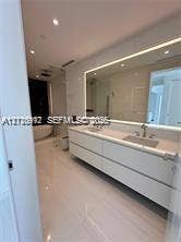 Floating dual-sink vanity with matte finishes, quartz countertop, large backlit mirror, and freestanding soaking tub