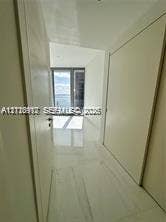 Hallway featuring large-format light-toned flooring, minimalist door frames, and floor-to-ceiling glass paneling
