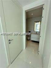 Solid-core white interior door with a contemporary metallic handle, polished tile flooring, wall-mounted floating vanity with integrated basin, and illuminated wall mirror