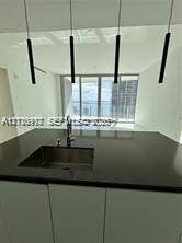 Modern kitchen island featuring a solid-surface countertop, integrated stainless steel undermount sink, gooseneck faucet, and four cylindrical pendant lights