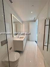 Modern bathroom featuring floor-to-ceiling tile, a floating dual-sink vanity with integrated lighting, a wall-mounted toilet, and a glass-enclosed shower