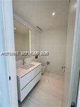 Wall-mounted white vanity with a rectangular integrated sink, stone countertop, large-format tile flooring, and a full-height backlit mirror