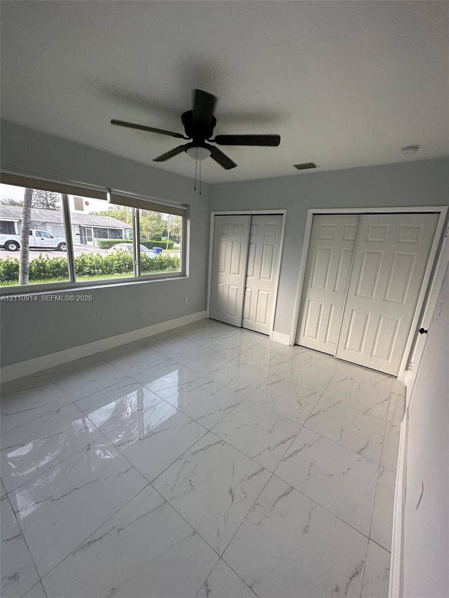 Large-format tile flooring with veining detail, multi-panel sliding closet doors, and a ceiling fan with integrated lighting