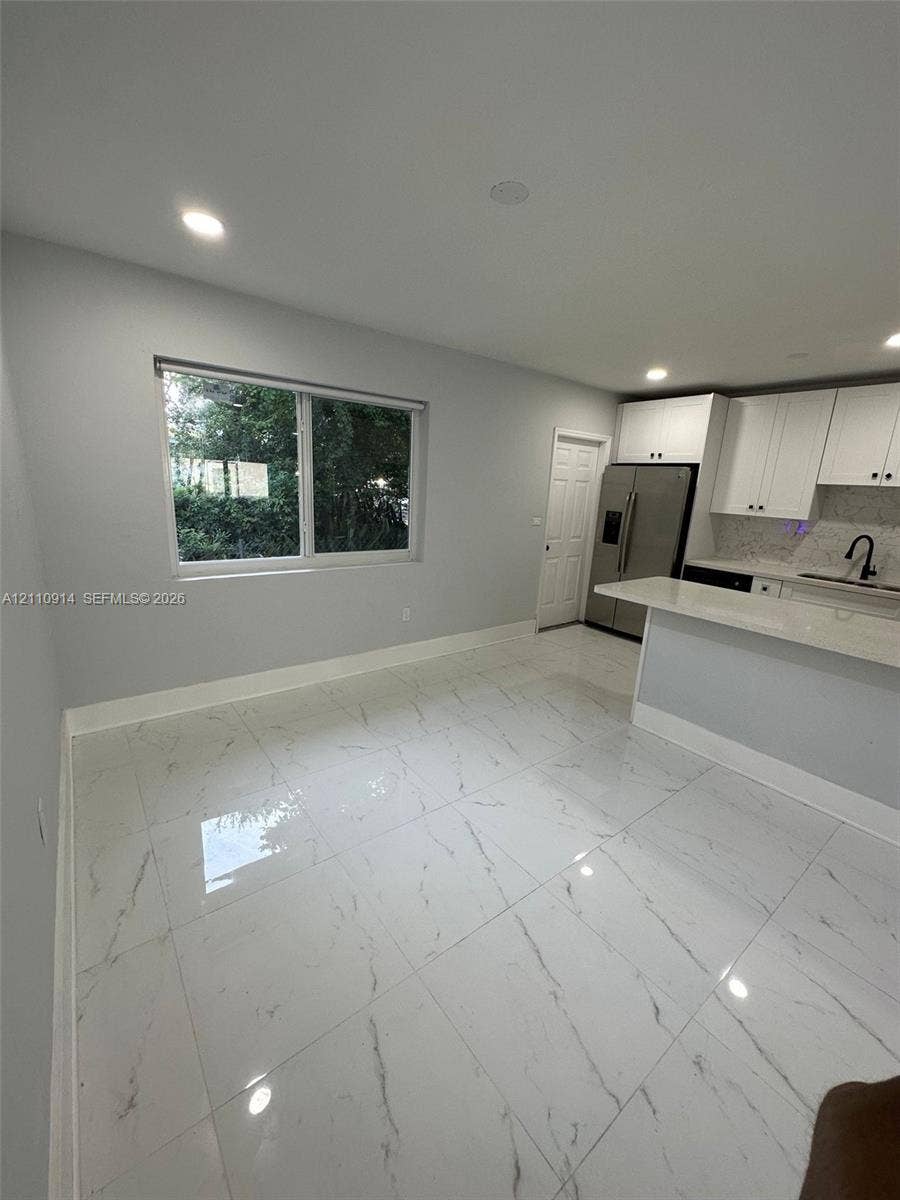 Large-format tile flooring with a neutral-veined finish, white shaker-style cabinetry, quartz countertops, and recessed lighting