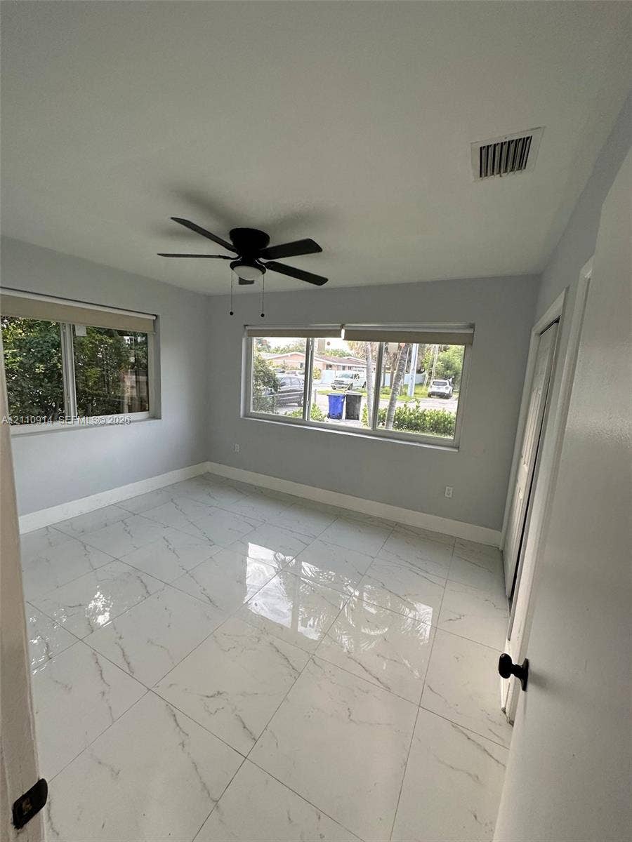 Large-format, polished stone-finish floor tiling featuring grey veining, ceiling fan with integrated lighting, and multiple windows with roller shades