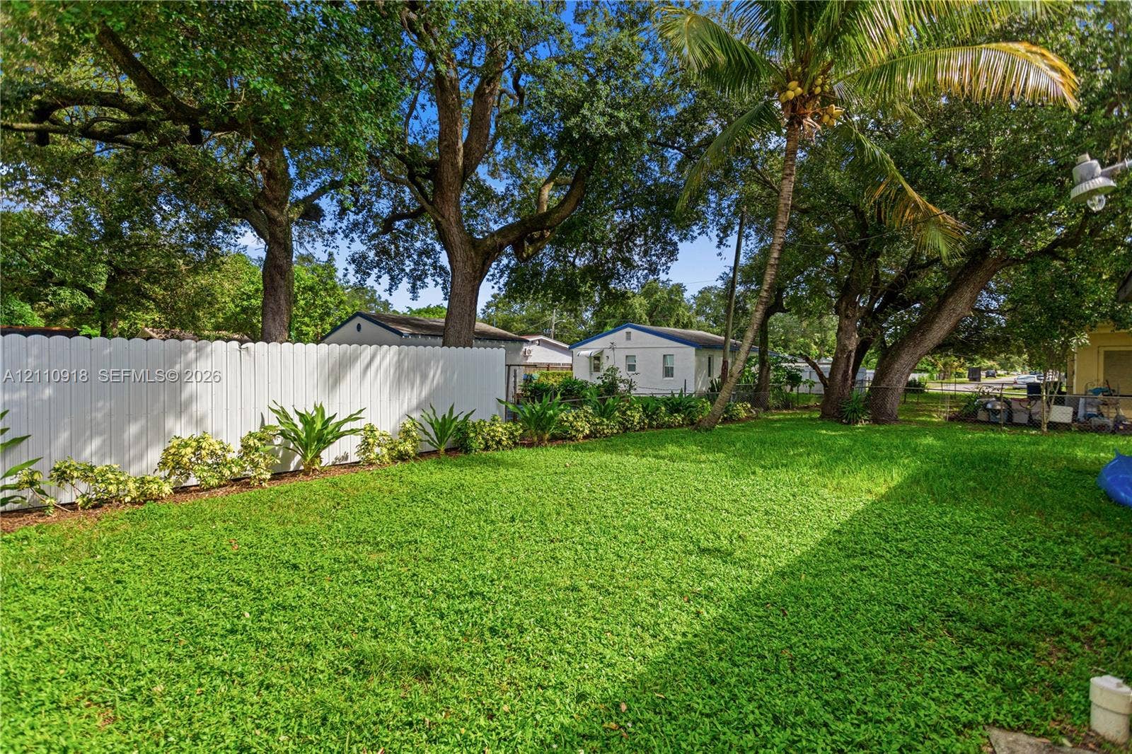 2007 NW 89th Street, Miami, FL 33147 Spacious backyard featuring a white vinyl privacy fence, mature trees, established palms, and a manicured lawn