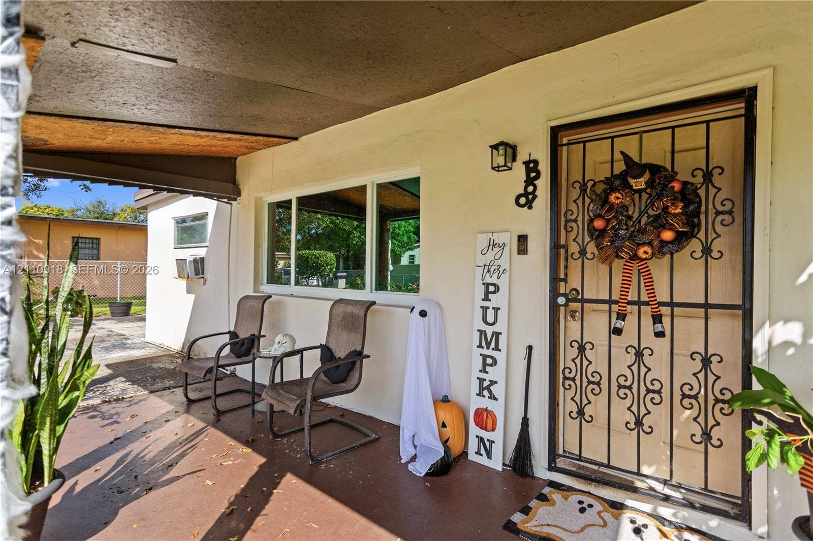 2007 NW 89th Street, Miami, FL 33147 Covered front porch featuring a decorative wrought-iron security door, smooth stucco exterior finish, and wall-mounted exterior lighting