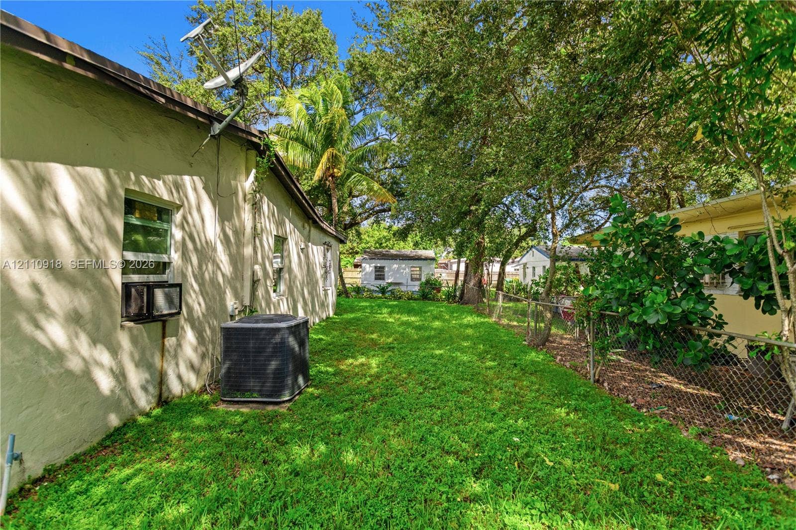 2007 NW 89th Street, Miami, FL 33147 Side yard featuring a grass lawn, chain-link perimeter fencing, and mature trees