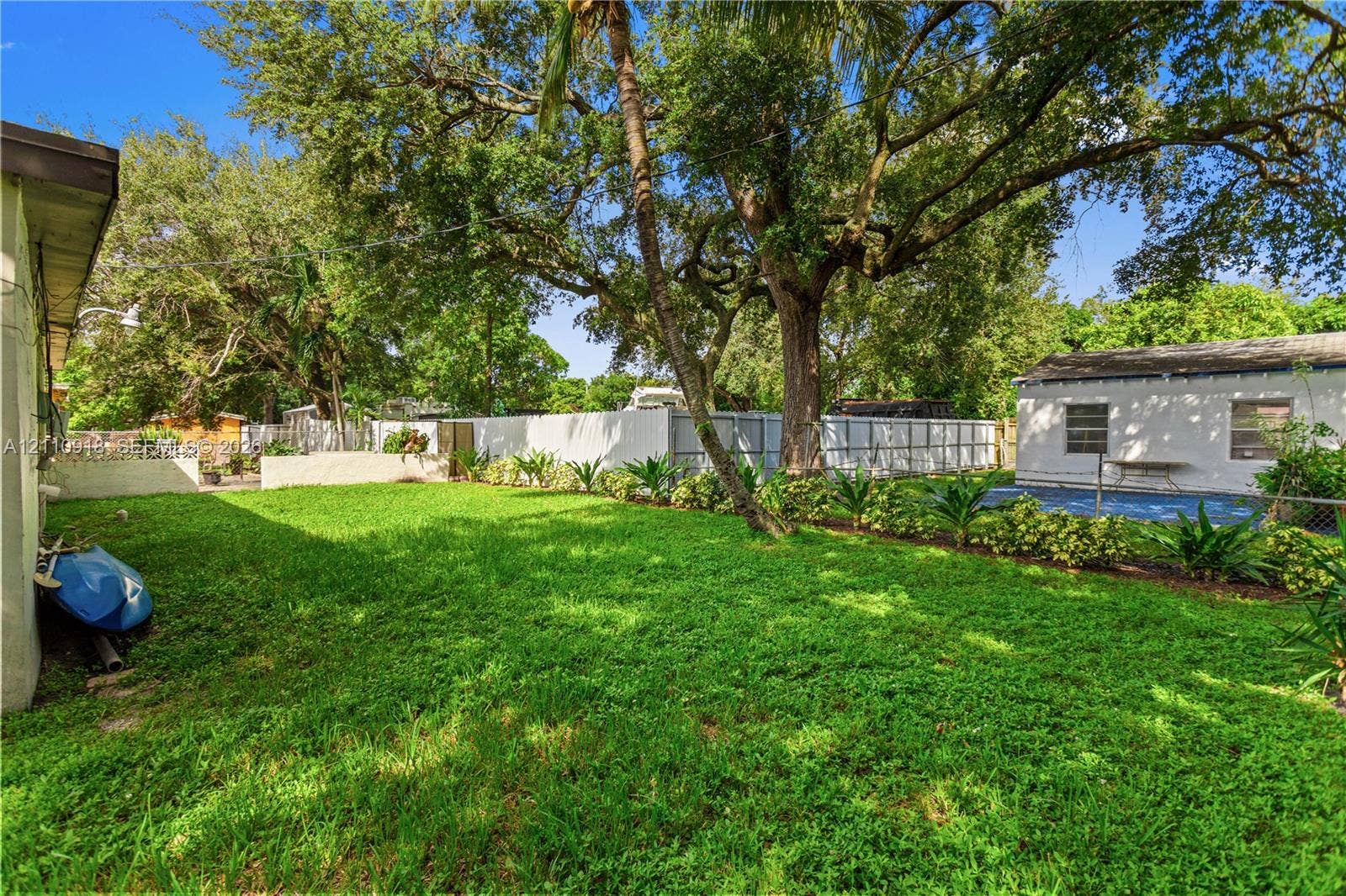 2007 NW 89th Street, Miami, FL 33147 Expansive backyard featuring a manicured lawn, mature trees, privacy fencing, and a swimming pool