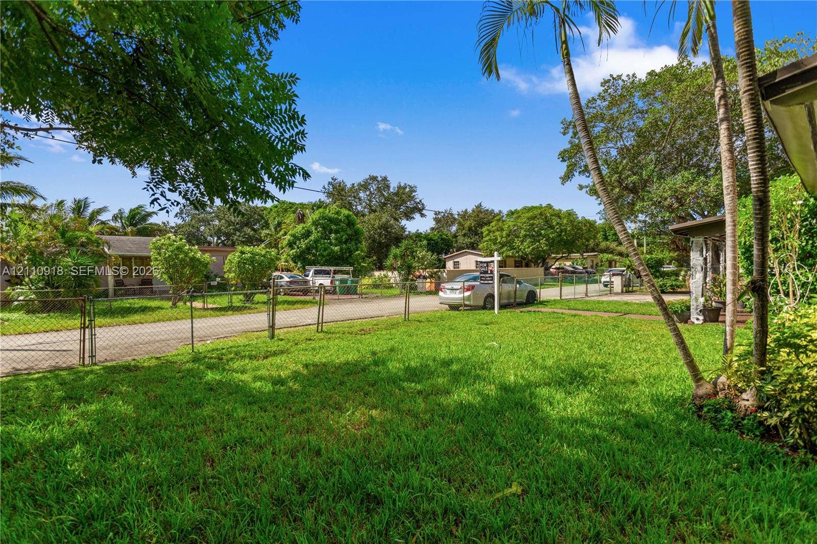 2007 NW 89th Street, Miami, FL 33147 Expansive front lawn featuring mature palm trees and perimeter chain-link fencing
