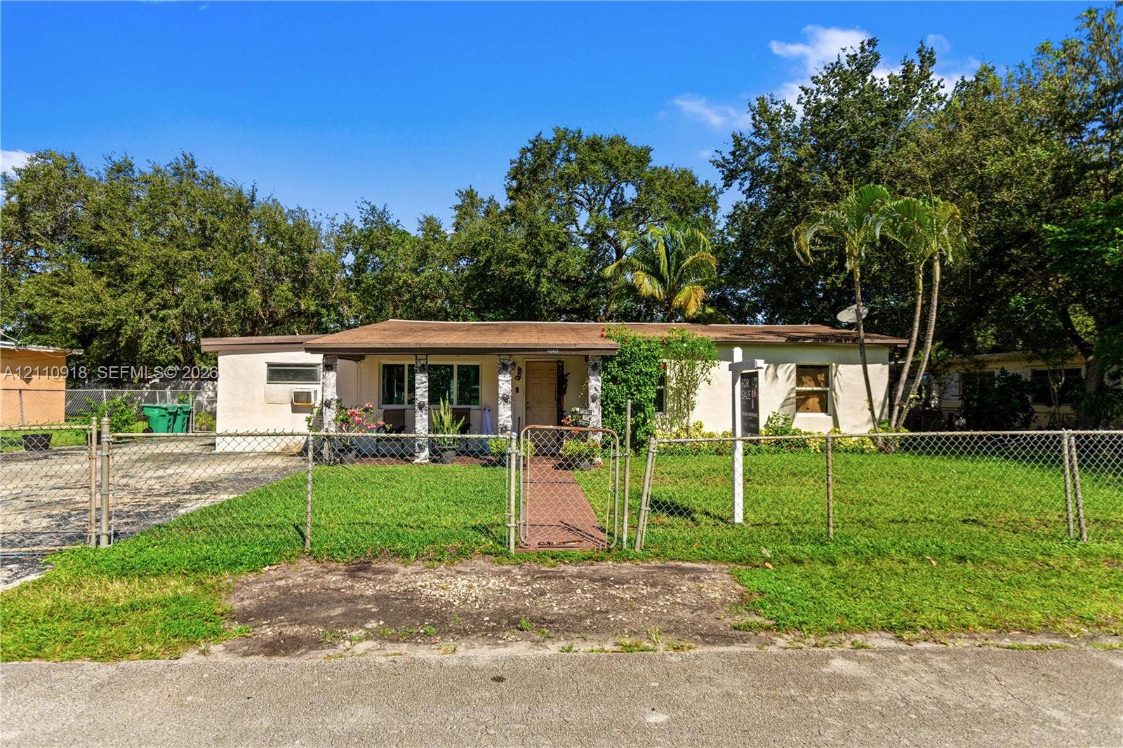 2007 NW 89th Street, Miami, FL 33147 Single-story exterior featuring a covered front porch, stone-column detailing, paved walkway, and a chain-link fenced perimeter