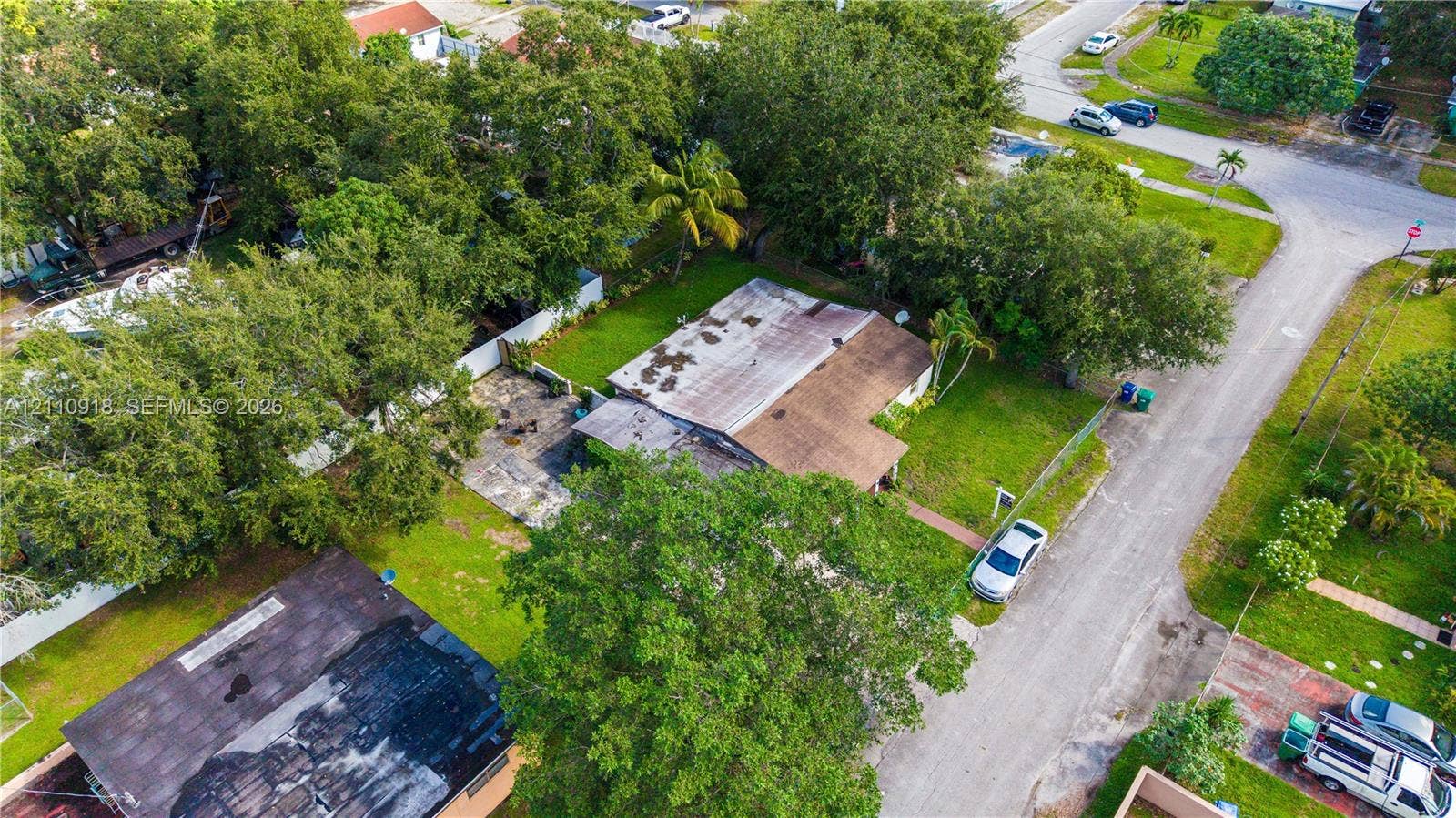 2007 NW 89th Street, Miami, FL 33147 Aerial perspective of a corner lot featuring established mature trees, a designated concrete patio, and a shingled roof exterior