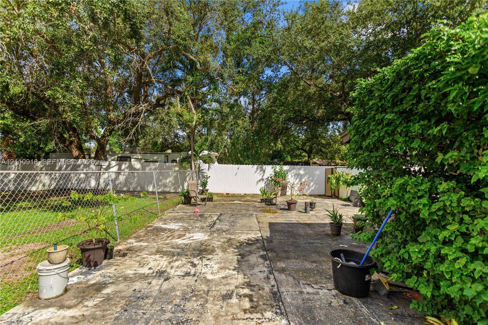 2007 NW 89th Street, Miami, FL 33147 Backyard featuring a concrete patio, perimeter chain-link and privacy fencing, and mature canopy trees