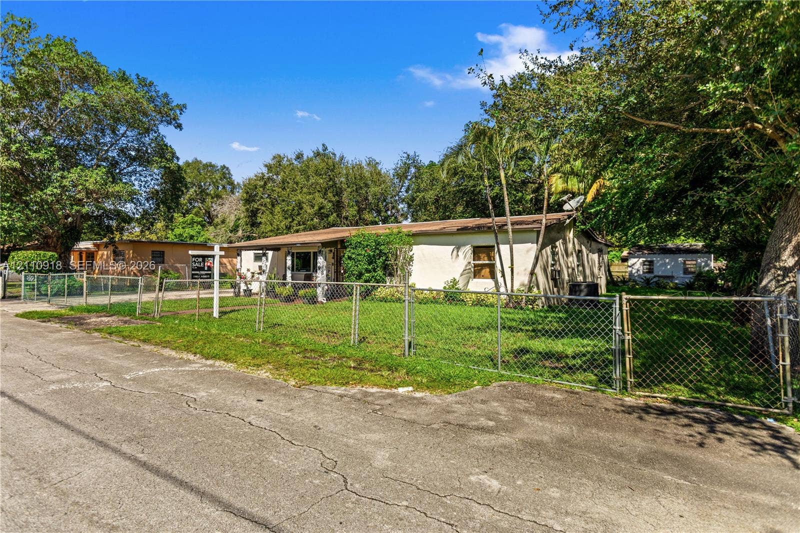 2007 NW 89th Street, Miami, FL 33147 Single-story exterior with a stucco finish, metal roof, chain-link perimeter fencing, and mature trees