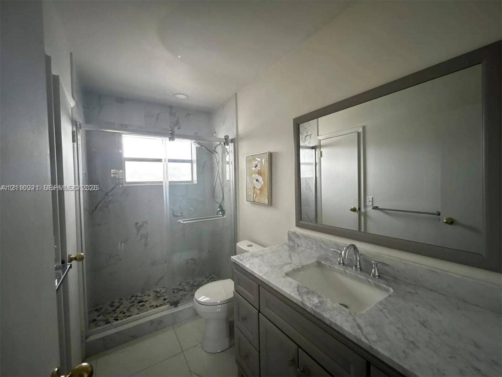 5003 NW 35th Street, #506, Lauderdale Lakes, Lauderdale Lakes, FL 33319 Bathroom featuring a stone-surface vanity with an integrated basin, a large framed wall mirror, a glass-enclosed shower with tiled walls, and stone-tile flooring