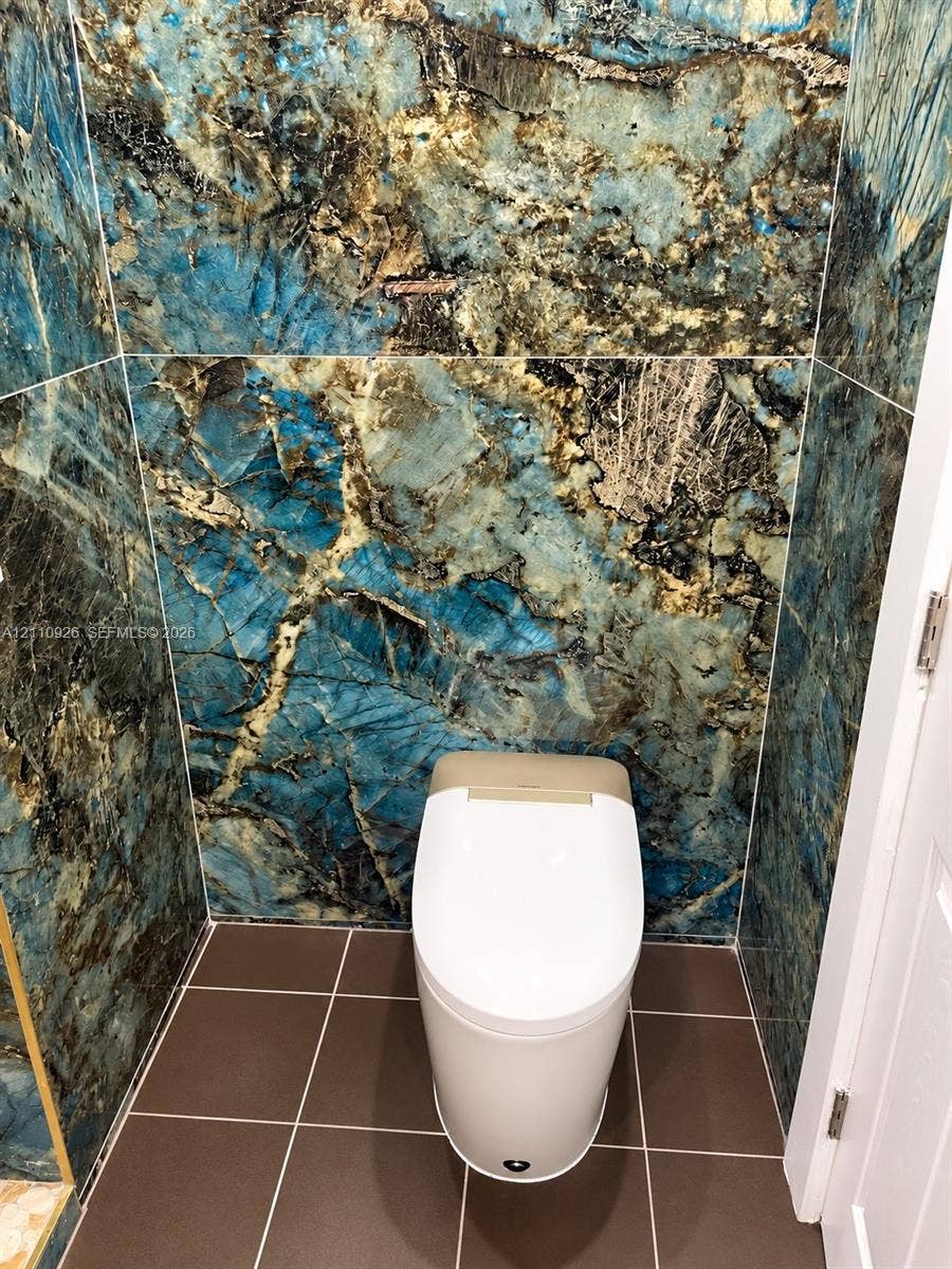 Full-height blue stone-finish wall cladding, minimalist white one-piece toilet, and large-format ceramic floor tiles