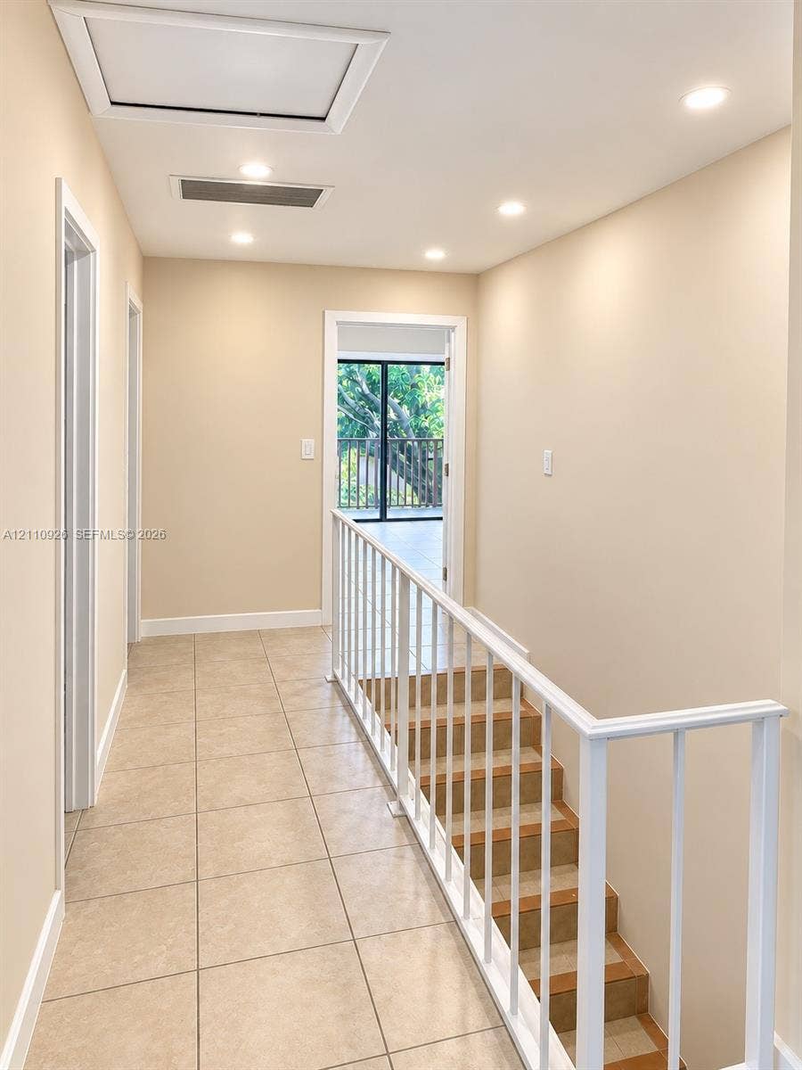 Hallway featuring neutral-toned tile flooring, recessed ceiling lighting, and a white metal railing staircase